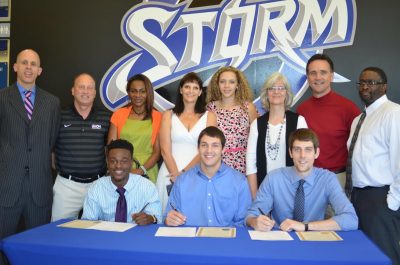 Three players signing with supportive group behind them