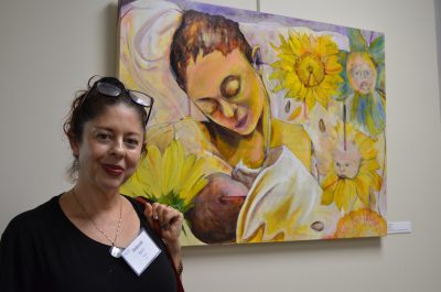 Artist Deborah Kern stands beside her oil painting of a mother holding a child.