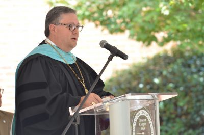 Dr. Darrin Hartness standing at podium in commencement attire