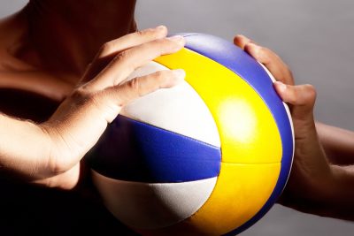 Individual holding blue, yellow and white volleyball
