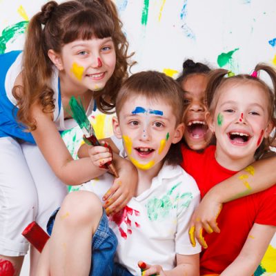 Young children holding paint brushes with paint on their clothes and faces