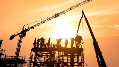 Workers on skyscraper being built with sun setting in background