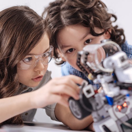 Two children looking intently at small robotic equipment