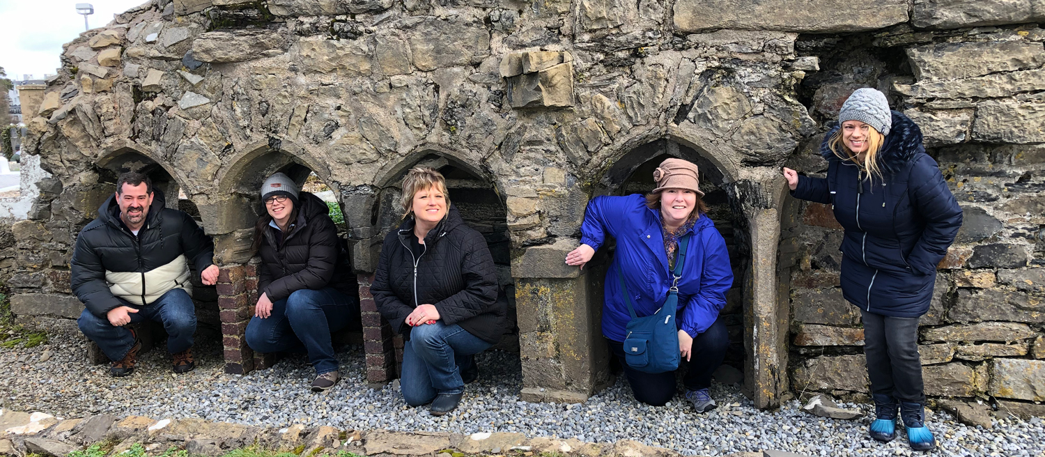 5 travelers dressed in warm clothes nestled under ancient architectural structure