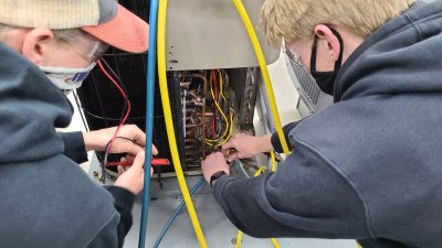Two male HVAC Students look at wiring of HVAC unit