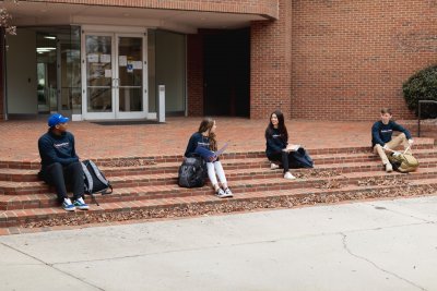 Four Students in Davidson-Davie shirts sitting distanced from each other on brick steps