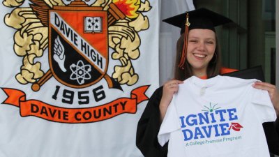 Cassidy Kluttz holding up Ignite Davie shirt in front of Davie County High School banner