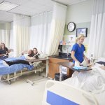 Nurses in Blue scrubs check on mock patients in hospital beds