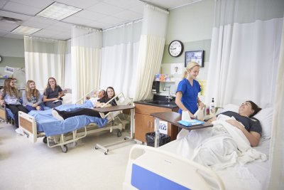 Nurses in Blue scrubs check on mock patients in hospital beds