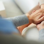 Closeup of an individuals hands comforting another person by holding their hands.