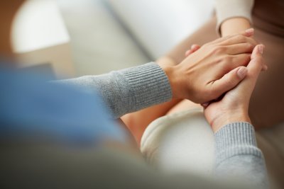 Closeup of an individuals hands comforting another person by holding their hands.
