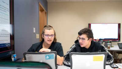 Two studnets look at laptops in classroom