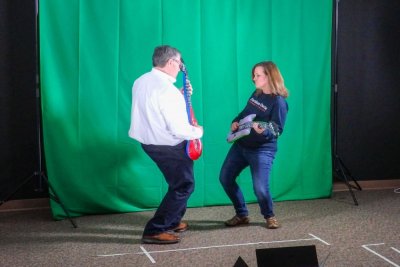 Two faculty members play inflatable guitars in front of green screen
