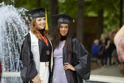 Two graduates in cap an gown pose in front of fountain