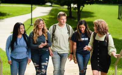 Five students walk in horizontal line toward camera