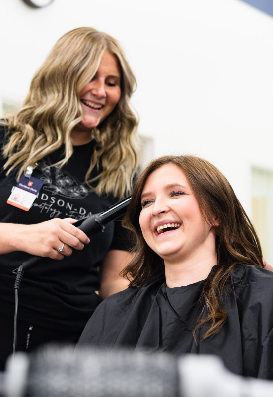 Cosmetology students smile and laugh while styling hair