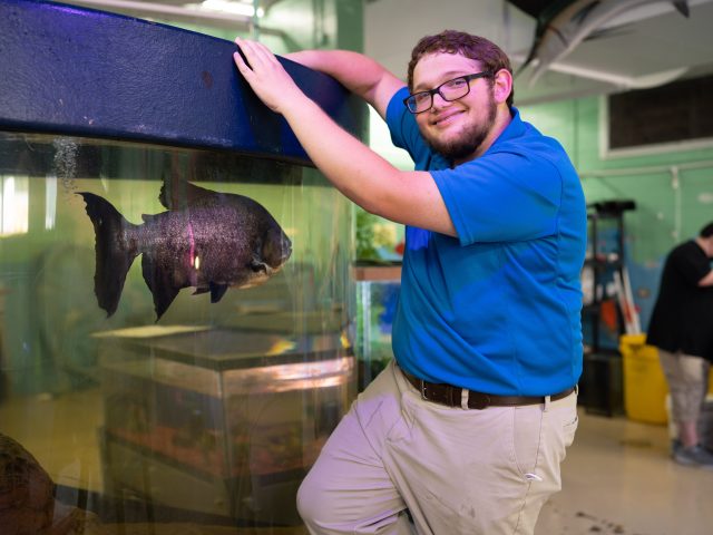 Aquarium Student poses in front of large fish in tank