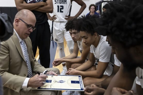 Storm Basketball Coach draws up play while team watches