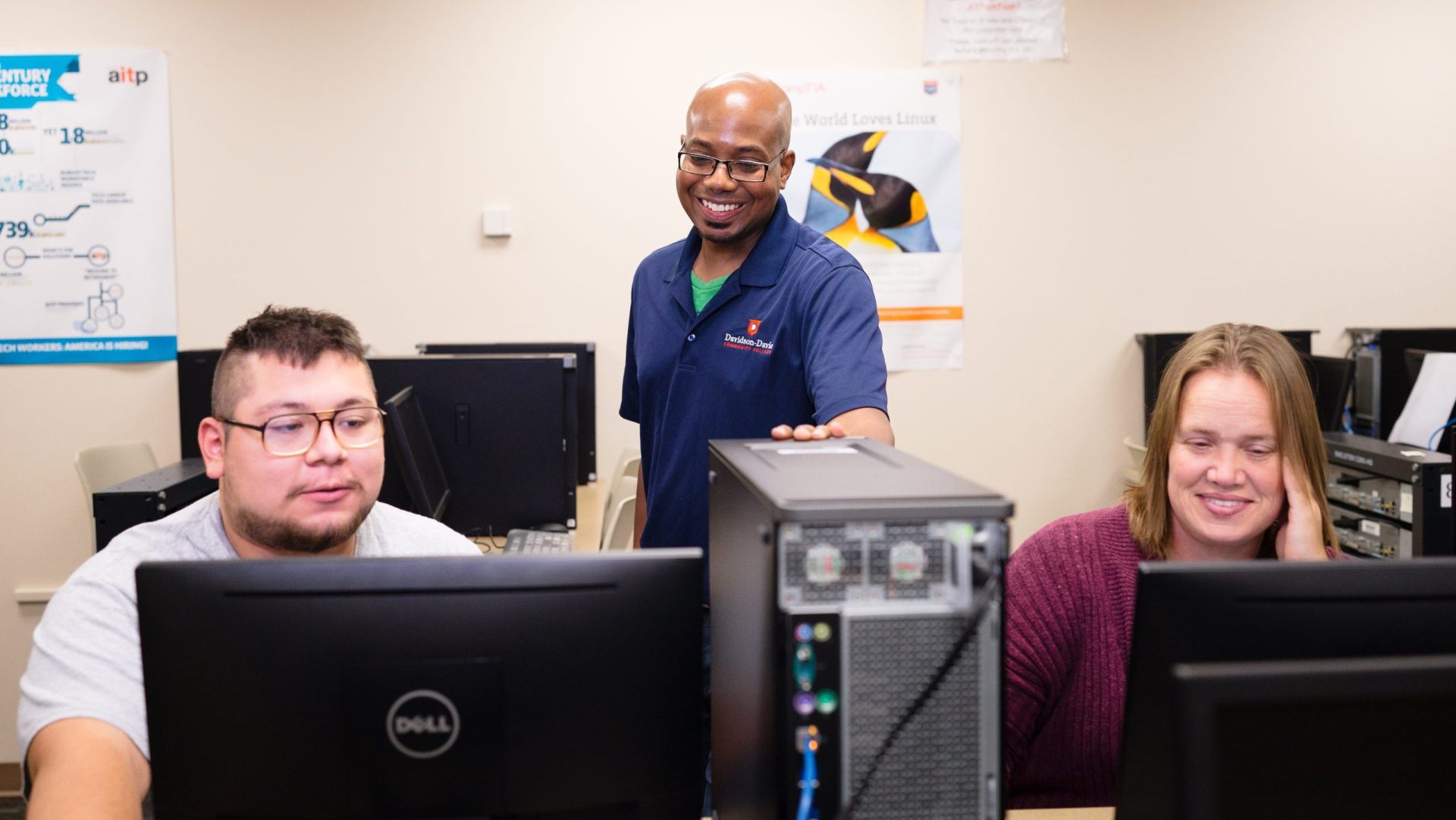 Information Technology Instructor helps two students at computers