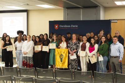 A diverse group of people at an award ceremony at Davidson-Davie Community College, holding certificates and a banner.
